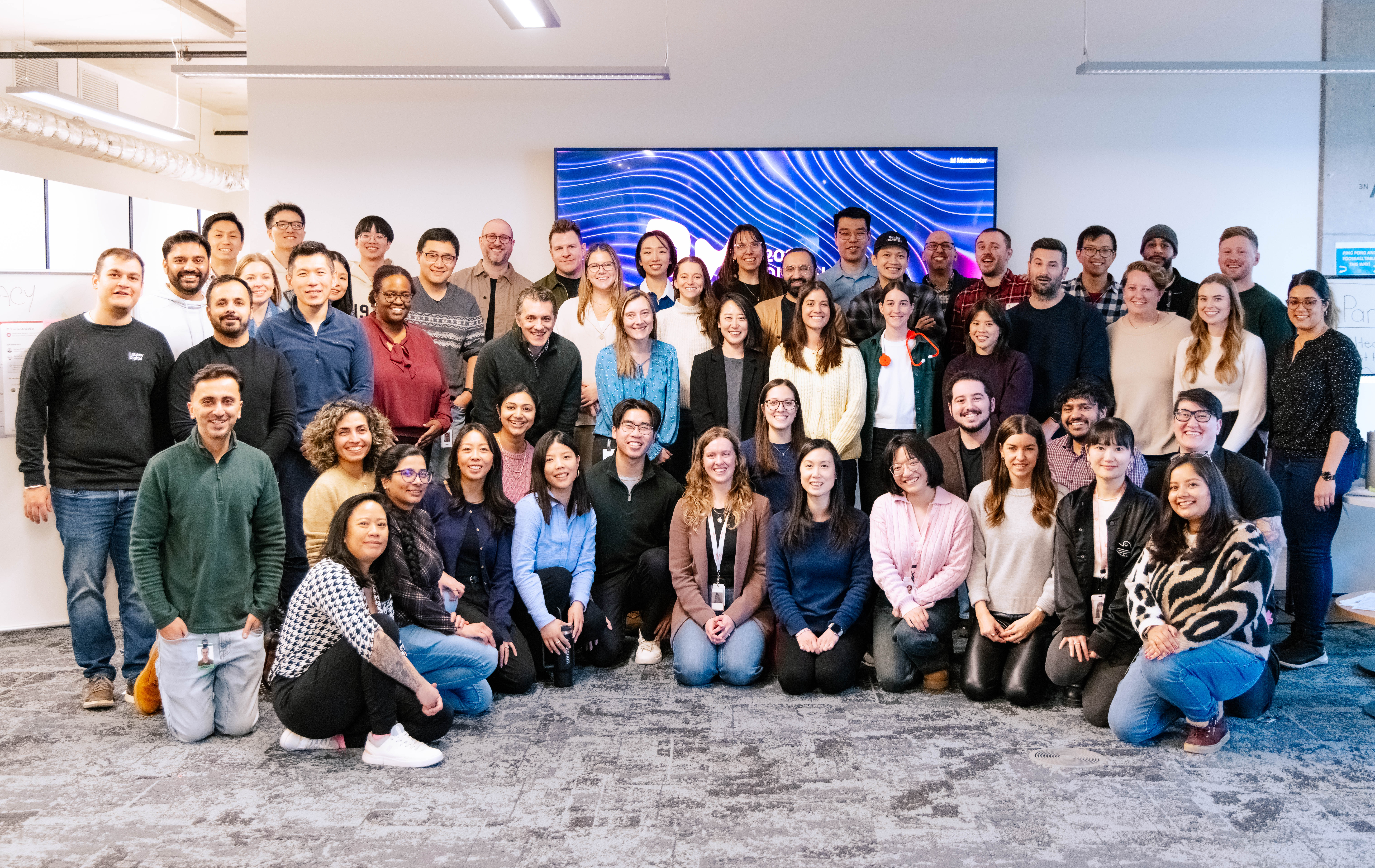Group photograph of the Loblaw Digital health team in their Toronto office, posed in front of a large screen.